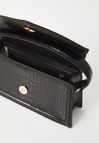 Black textured faux leather handbag with a gold snap closure, interior zip pocket, and a slim handle.