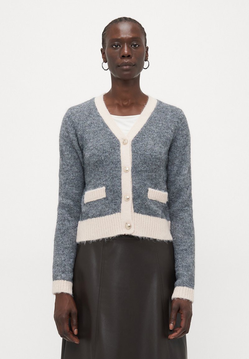 Cardigan grigio e beige chiaro con scollo a V, bottoni perle, due tasche frontali e polsini e orlo a coste. Materiale in maglia con una texture morbida.