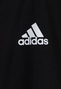 Tissu noir arborant un grand logo blanc d'Adidas avec trois rayures diagonales au-dessus du mot "adidas", en gras et clairement visible sur le fond.