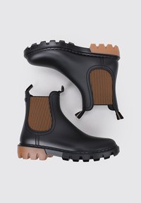 Bottes Chelsea en caoutchouc noir avec des panneaux latéraux rayés bruns, des semelles texturées et des languettes pour un enfilage facile, présentant une conception robuste et imperméable.