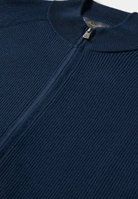 Námořnické modré žebrované pletené svetr s vysokým límcem a částečně rozepnutým stříbrným zipem.