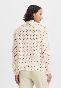 Light peach blouse with black polka dots, pleated texture, long sleeves, and a collar. The back view shows a relaxed fit and soft fabric.
