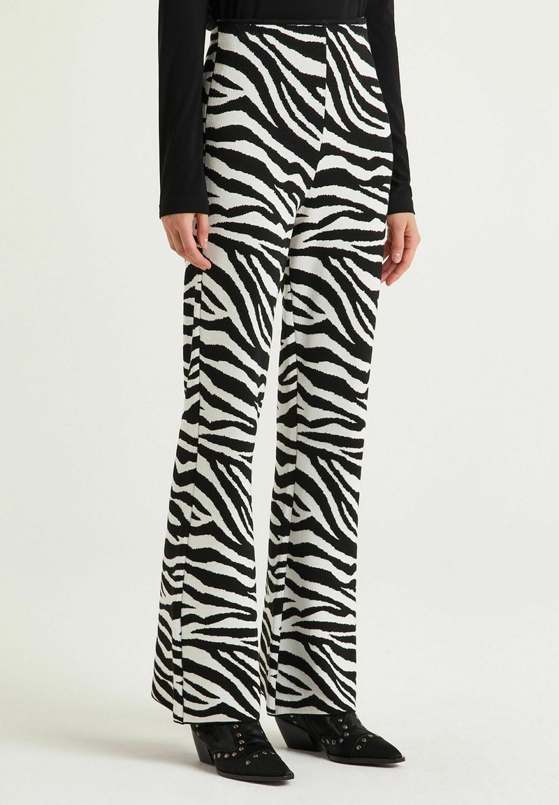 Pantalon patte d'éléphant ajusté à imprimé zèbre noir et blanc avec un tissu texturé et une taille haute, associé à des bottines noires à talons.