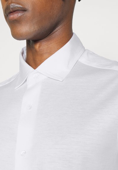 Cămașă albă cu mânecă scurtă, cu guler clasic, fabricată dintr-un material neted. Prezintă un închidere prin butoni și un design minimalist fără modele.