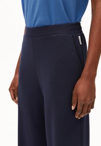 Marinblå atletiska byxor med en elastisk midja, sidofickor och en mjuk yta. Materialet verkar lätt och andningsbart.