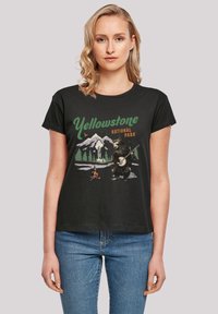 Schwarzes Baumwoll-T-Shirt mit einem grafischen Druck eines Bären, der Banjo spielt, mit Bergen und Bäumen, beschriftet mit "Yellowstone Nationalpark."