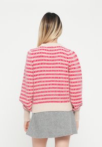 Sweter dzianinowy z bufiastymi rękawami, z teksturowanym wzorem różowych i czerwonych kwadratów na beżowym tle. Żebrowane wykończenie u dołu i na rękawach.