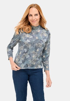 Haut à manches longues imprimé floral en bleu, vert et crème, fabriqué en tissu doux avec un col rond et une coupe décontractée. Associé à un jean foncé.