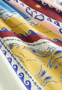 Tissu avec des couches pliées présentant des motifs ornés en jaune, bleu, rouge, rose et blanc, comprenant des volutes, des formes florales et des motifs de soleil.