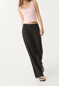 Zwarte broek met wijde pijpen en een strakke vormgeving, met een gladde textuur en voorzakken, gecombineerd met een lichtroze aansluitend tanktop.