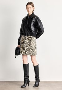 Melnas ādas bomber jaka ar ribveida aprocēm, leoparda raksta svārki ar loku detaļu. Melnas ceļgalu augstpapēžu zābaki un neliela melna soma.