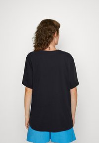 Black cotton t-shirt with short sleeves, relaxed fit, and rounded neckline, showing back view with hemline curving gently.
