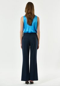 Koboltblå satin sleeveless top parret med navy flared bukser, der har lommer, glat tekstur og diskrete detaljer ved taljen.