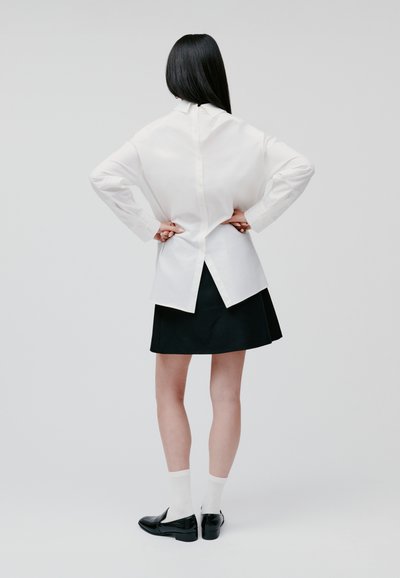 White button-up shirt with a back split, paired with a black skirt. Black loafers and white socks complete the outfit. Minimalist design.