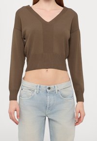 Pull court marron avec ourlet côtelé et manches longues ; présente un col en V profond et une texture lisse, porté avec un jean taille haute bleu clair.