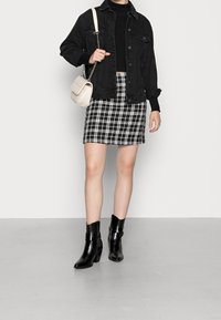 Svart denimjacka över en svart polo, tillsammans med en rutiga minikjol och svarta ankelskor. Har även en ljusbeige axelremsväska.