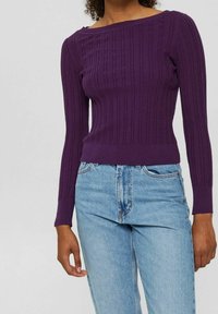 Lila ribbad långärmad topp med vid halsringning och figurnära silhuett, kombinerad med ljusblå högmidjade jeans.