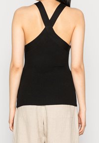 Canotta nera a coste con spalline incrociate sul retro. Tessuto morbido, design aderente e orlo dritto. Abbinata a pantaloni di colore chiaro.