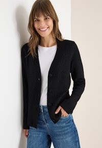 Cardigan nero lavorato a maglia con scollatura a V, cinque bottoni e texture a coste, indossato sopra una maglietta bianca e abbinato a jeans blu.
