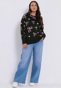 Musta neule, jossa on vaaleanpunaiset nauhat ja sydämen kuvioita, rento malli ja ribbireunat. Yhdistetty leveälahkeisiin farkkuihin ja valkoisiin lenkkarit.