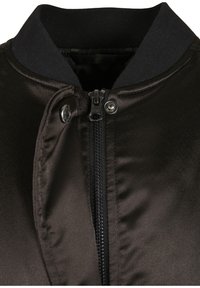 Blouson aviateur en satin noir avec fermeture éclair, détail à boutons-pression, et col côtelé. Le tissu texturé apporte une finition élégante.