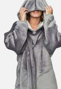 Grande sweat à capuche gris, avec une texture douce, comportant des poches avant et un doublure partielle en tartan. La capuche obscurcit le visage.