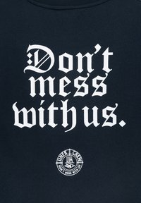 Tmavě modrá mikina s výrazným bílým textem: "Neruš nás." Kruh logo pod ním uvádí "UNFR CREW." Měkký bavlněný materiál.