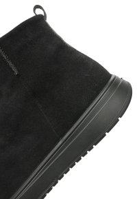 Black suede ankle boot with loop pull tab, stitched seam, and thick textured rubber sole shown in close-up.