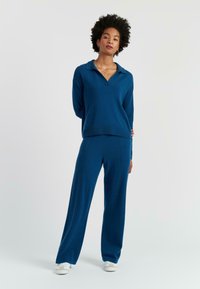 Blauwe gebreide pullover met een kraag, gecombineerd met bijpassende rechte broeken met een zachte textuur en minimalistische stikdetails.