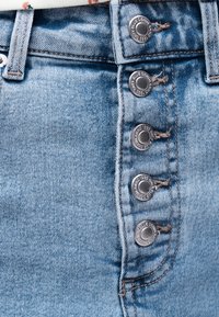 Close-up af lyseblå denimjeans forside med fem synlige metalknapper og bæltestropper.