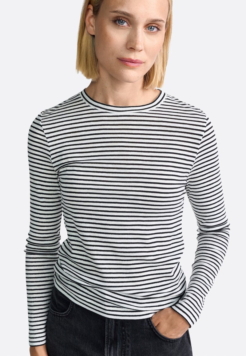 Langärmliges Shirt mit horizontalen schwarz-weißen Streifen, rundem Halsausschnitt und taillierter Silhouette, kombiniert mit dunklen Jeans.