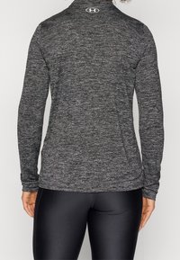 Langärmliges Sportoberteil aus schwarzem Melange-Stoff. Mit hohem Kragen, slim Fit und Logo in der Nähe des Ausschnitts. Glatte Textur und dehnbares Design.