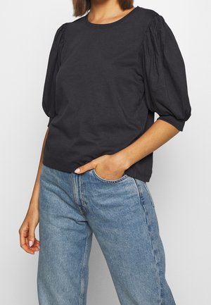 Haut noir à manches courtes avec des manches bouffantes, encolure arrondie et texture en coton doux. Associé à un jean taille haute bleu clair.
