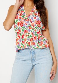Top envolvente floral con fondo blanco decorado con flores rojas, moradas y naranjas. Tiene un escote en V y un dobladillo con volantes, combinado con jeans claros.