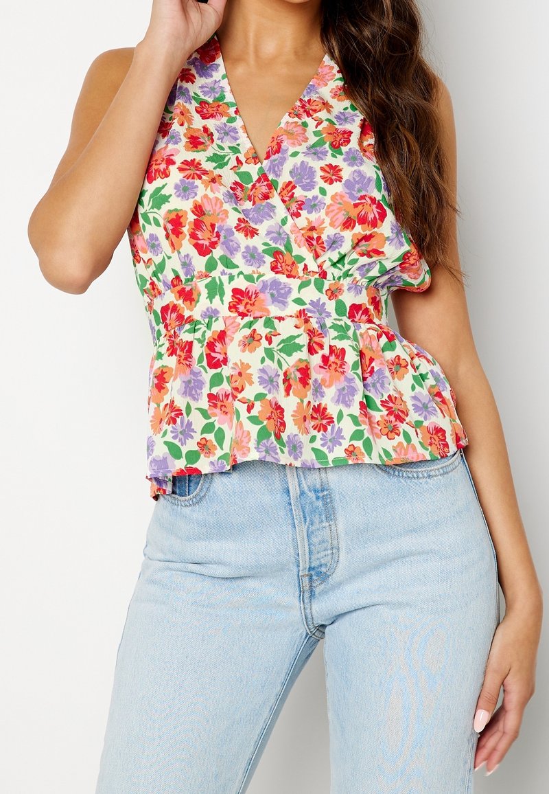 Top envolvente floral con fondo blanco decorado con flores rojas, moradas y naranjas. Tiene un escote en V y un dobladillo con volantes, combinado con jeans claros.