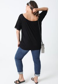 Zwart shirt met korte mouwen en kantafwerking, gecombineerd met opgerolde blauwe jeans. Geaccessoireerd met een zilveren schoudertas en zwarte slippers.