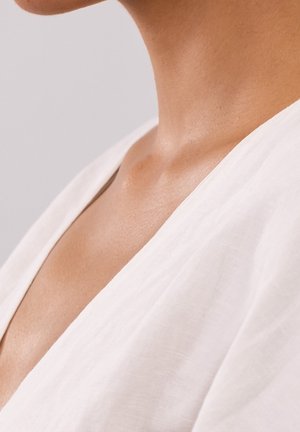 Vêtement en lin blanc avec un décolleté en V profond, une texture douce, et un ton de peau lisse visible le long du décolleté.