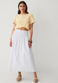 Lys gul, eyelet crop top med korte ærmer og rund halsudskæring, bÃ¥ret med en hvid, smocket talje maxi nederdel og beige platform sandaler.