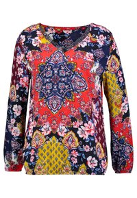 Monivärinen pitkähihaiset paita, jossa on V-pääntie, kukka- ja geometrisia kuvioita punaisena, sinisenä, keltaisena ja valkoisena tummalla taustalla.