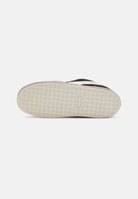 Tenis negri cu o talpă texturată, având un model distinctiv în formă de diamant. Vederea de jos evidențiază materialul de cauciuc și detaliile de cusătură.