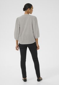 Gray, textured blouse with puff sleeves, paired with black slim-fit pants and flat shoes, shown from the back. Plain, neutral background.