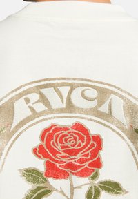 Camiseta blanca con un gran gráfico de rosa dorada y roja y el texto "RVCA" en un estilo vintage. Tejido suave con un diseño clásico de cuello redondo.