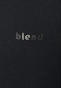 Camiseta negra de tela suave con un acabado texturizado; presenta la palabra "blend" en una combinación de letras negras y plateadas.