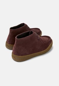 Bordeauxfarbene Wildleder-Stiefeletten mit runder Zehenpartie, ausgestattet mit einer Schnürung und einer strukturierten braunen Gummisohle. Minimalistisches Design ohne sichtbare Logos.