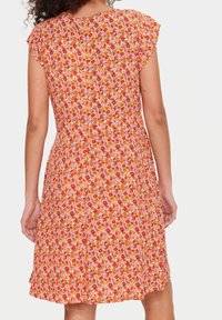 Kukkapuku vaaleanpunaisena, jossa on lyhyet hihat ja punaisia, oransseja ja vaaleanpunaisia kukkia. Kangas on kevyttä ja siinä on valuva helma.