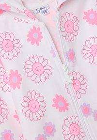 Monos de una pieza blancos con estampados de flores rosas y moradas, con capucha y un tirador de cremallera con forma de flor. Tejido suave con una textura lisa.