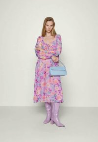 Vestido floral com mangas bufantes em tons de rosa, roxo e laranja; combinado com botas brilhantes lilás até ao joelho e uma mala azul-clara.