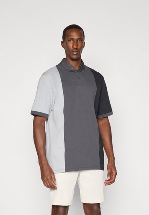 Polo de manga curta em blocos de cor cinza e cinza claro, feito de tecido de algodão, possui um decote com colarinho e uma pala de três botões.