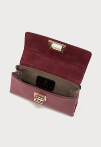 Carteira de couro bordô com interior em camurça, apresentando um fecho em tom dourado e etiqueta com marca. Duas divisões para organização.