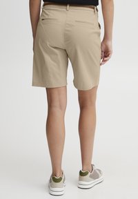 Khaki shorts med en glatt tekstur, midlår-lengde, og to baklommer. Kombinert med sporty sko med grønne detaljer.